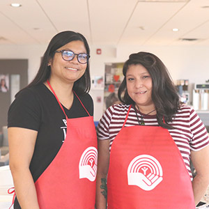 Two smiling Pay it forward volunteers standing side-by-side wearing UnitedWay aprons.